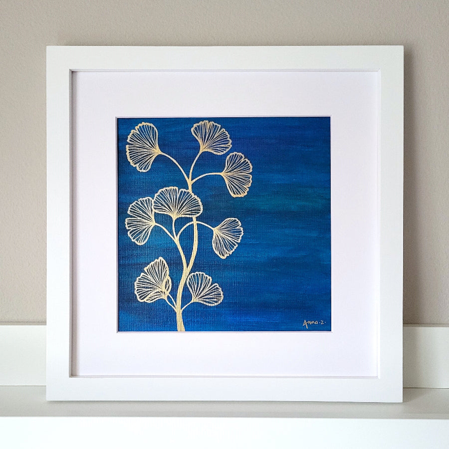 Stylized drawing of gingko leaves and branches in gold ink against a deep blue watercolor background, balancing richness and minimalism. Artwork is in a white wooden frame.