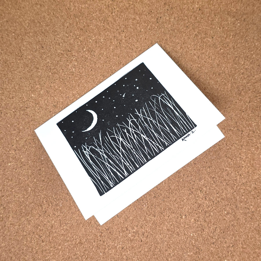 Notecard featuring a digital print reproduction of an original hand-carved block print artwork of a landscape with a crescent moon, starry sky and tall grasses. Black and white artwork.