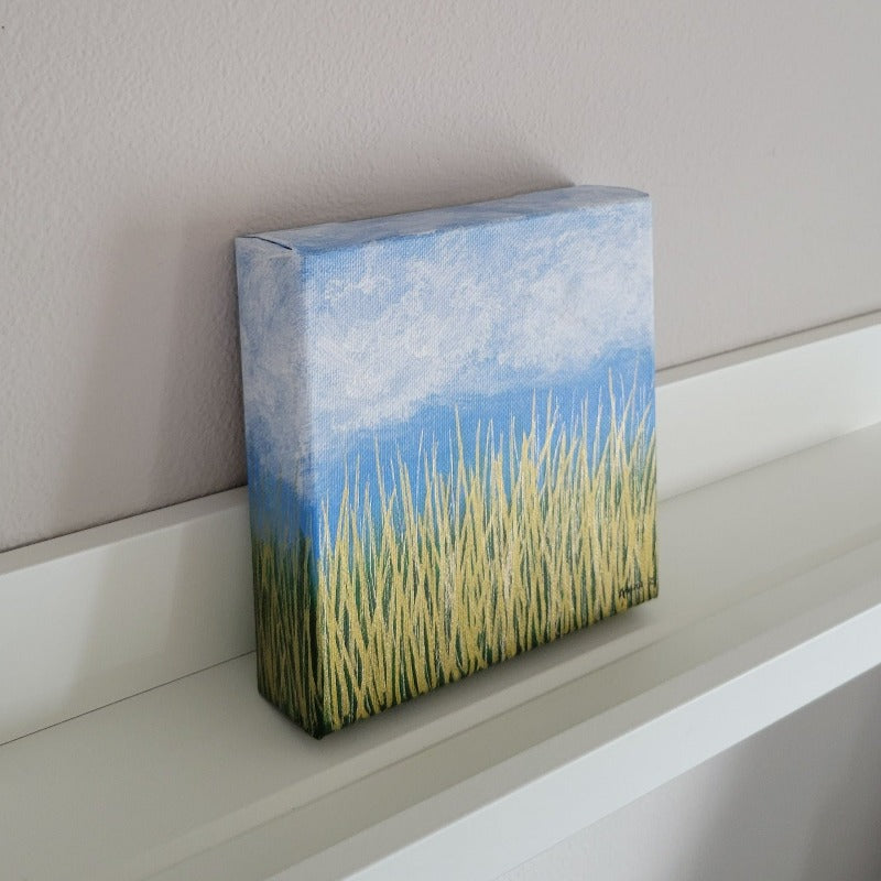 A dreamy mini painting of wispy white clouds against a bright blue sky, with golden grass below and a subtle green background in the distance. The metallic grass shines brilliantly especially in daylight. A cheerful piece capturing nature's beauty in simple details.