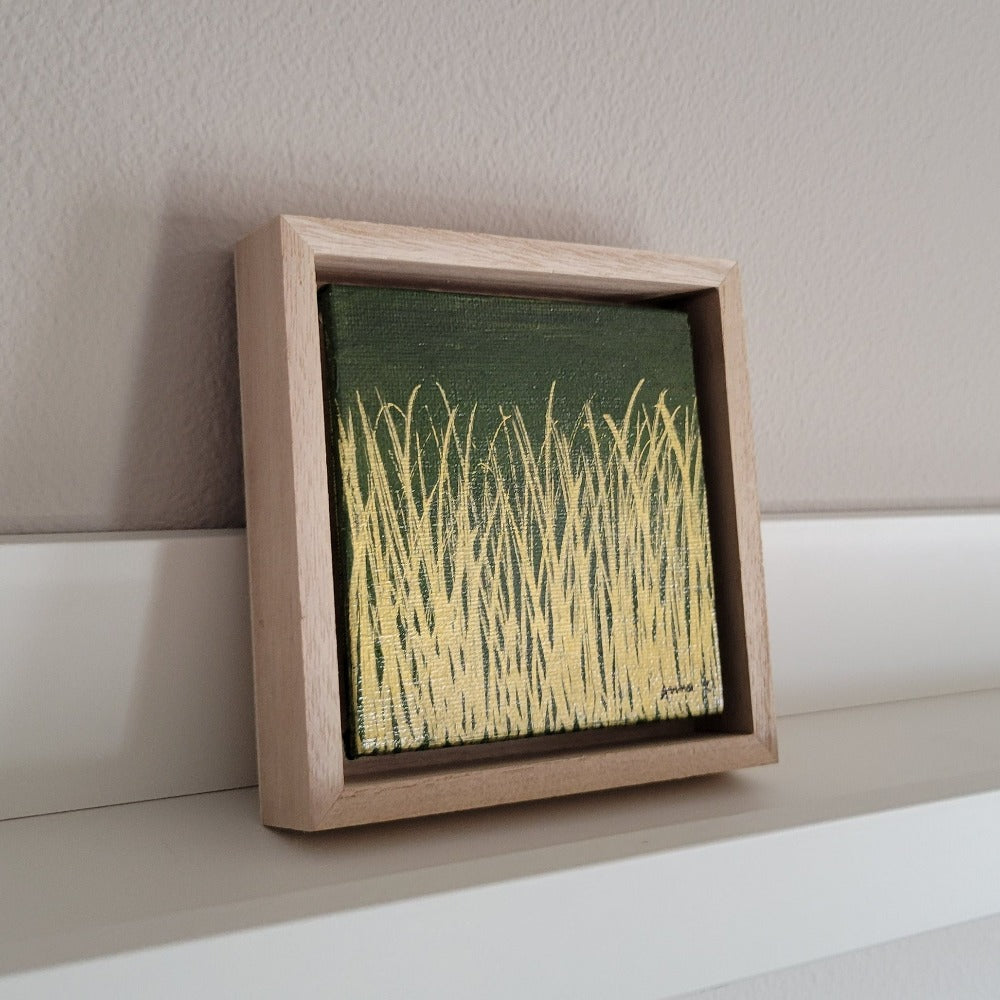 Golden blades of grass set against a deep moss green background on a framed mini-sized canvas panel. Metallic gold colored paint over acrylic. Mounted in floater frame style within a 5" x 5" rustic wooden box frame with mini sawtooth hanger on reverse. The golden grass catches daylight beautifully and is perfectly complemented by the light colored wooden frame.