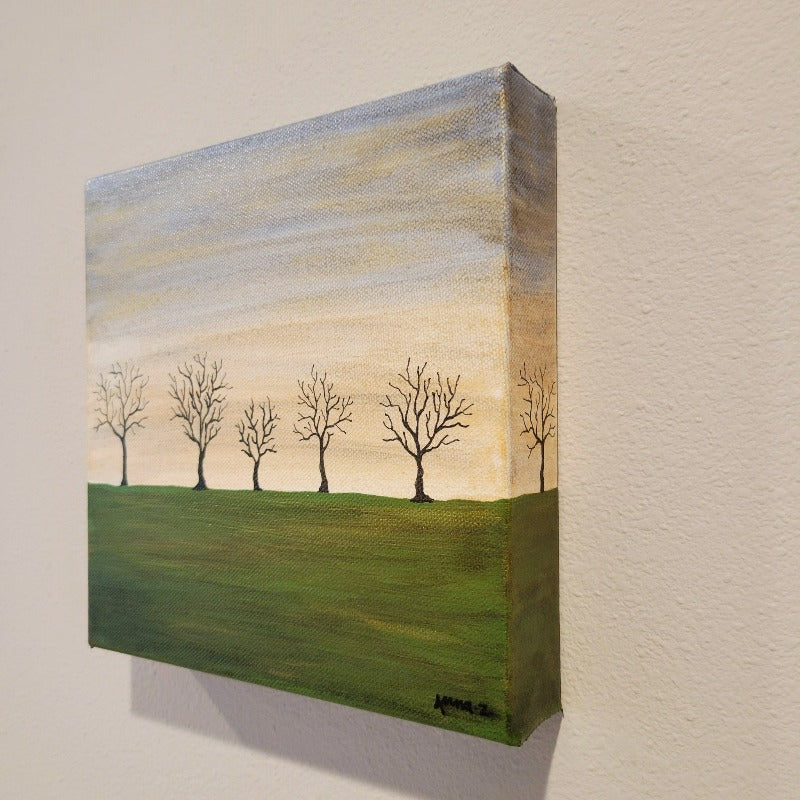 A dreamy landscape of bare trees against a golden twilight horizon and deep green fields. Subtle metallic highlights add interest and atmosphere.