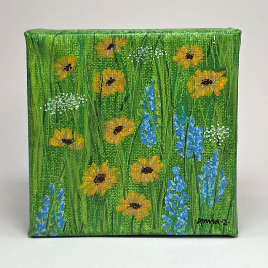 Front view of a mini painting of bright little sunflowers with their blue and white wildflower friends in the spring sunshine. A warm grassy meadow adds the perfect background for this joyful mini painting inspired by springtime in central Washington.