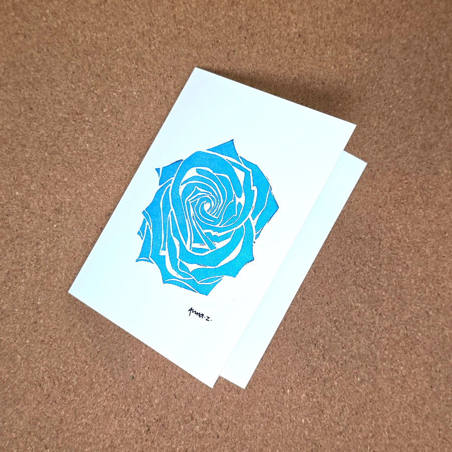 Notecard featuring a digital print reproduction of an original hand-carved block print artwork of a rose in blue on a white background.