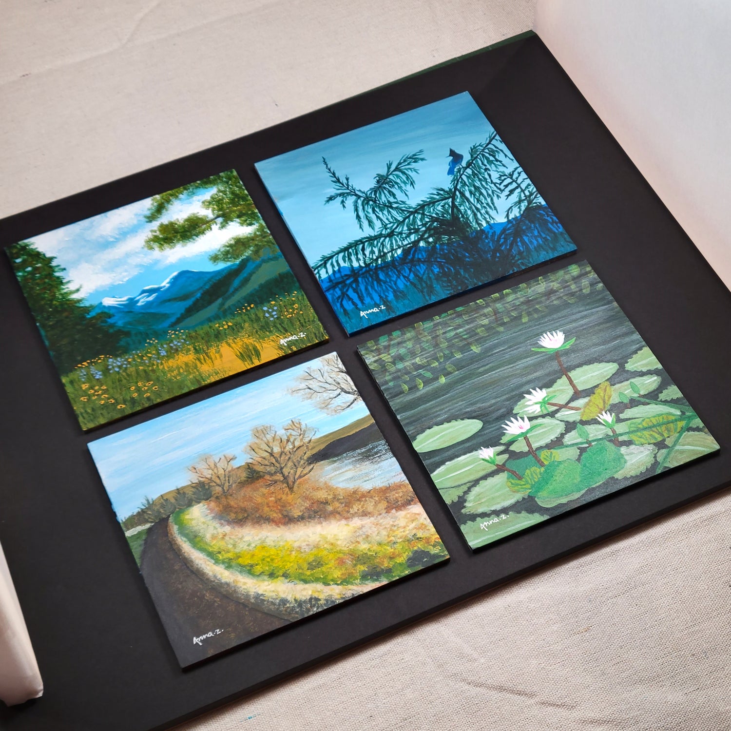Unframed versions of four miniature landscape paintings on panels, placed together on a black background