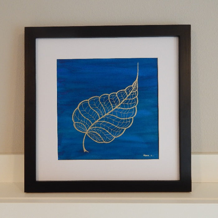 Original painting by Annazach Art. Stylized drawing of a banyan leaf in gold ink against a deep blue background with hints of green. In metallic ink set against a deep blue watercolor background with hints of green, this color combination creates a perfect balance of richness and minimalism. 