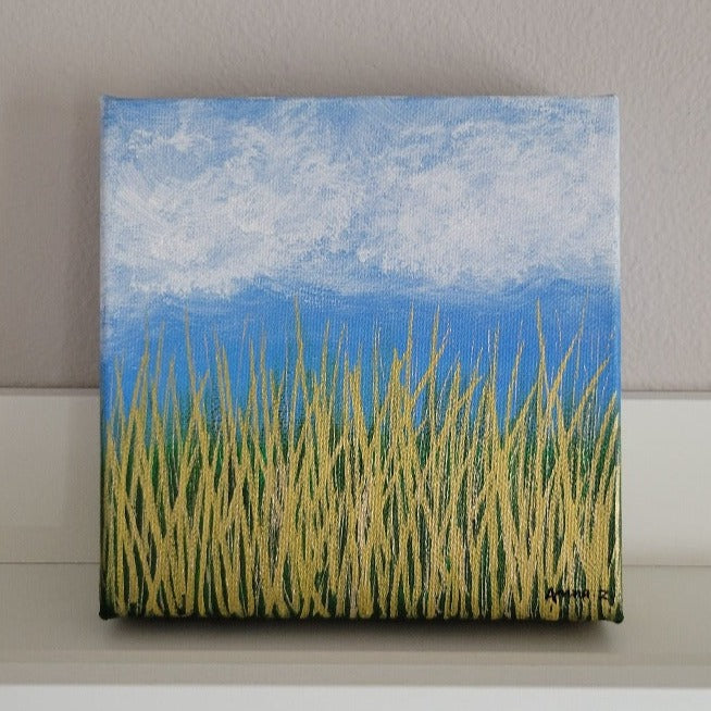 A dreamy mini painting of wispy white clouds against a bright blue sky, with golden grass below and a subtle green background in the distance. The metallic grass shines brilliantly especially in daylight. A cheerful piece capturing nature's beauty in simple details.