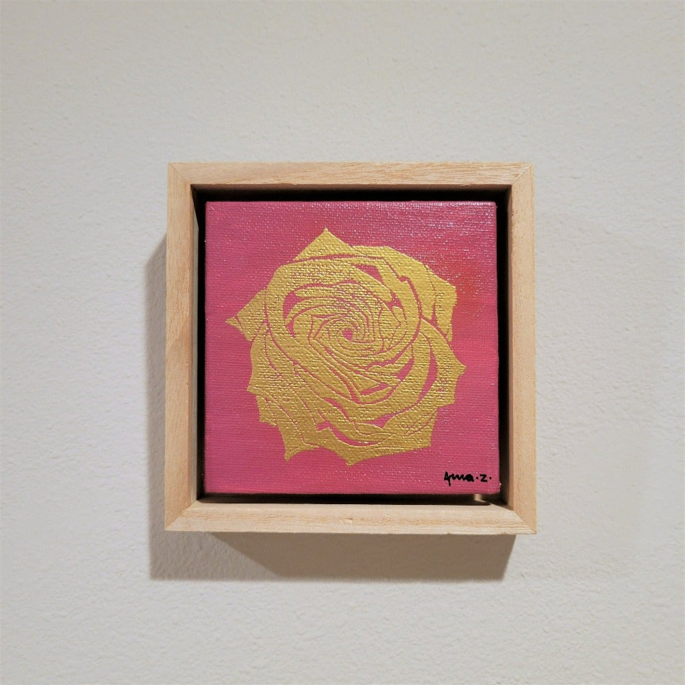 Golden rose set against a bright pink background on a framed mini-sized canvas panel. Metallic gold colored heat embossing from original carved block design, over an acrylic painted background.  Mounted in floater frame style within a 5" x 5" rustic wooden box frame with mini sawtooth hanger on reverse. The golden petals are perfectly complemented by the light colored wooden frame. 