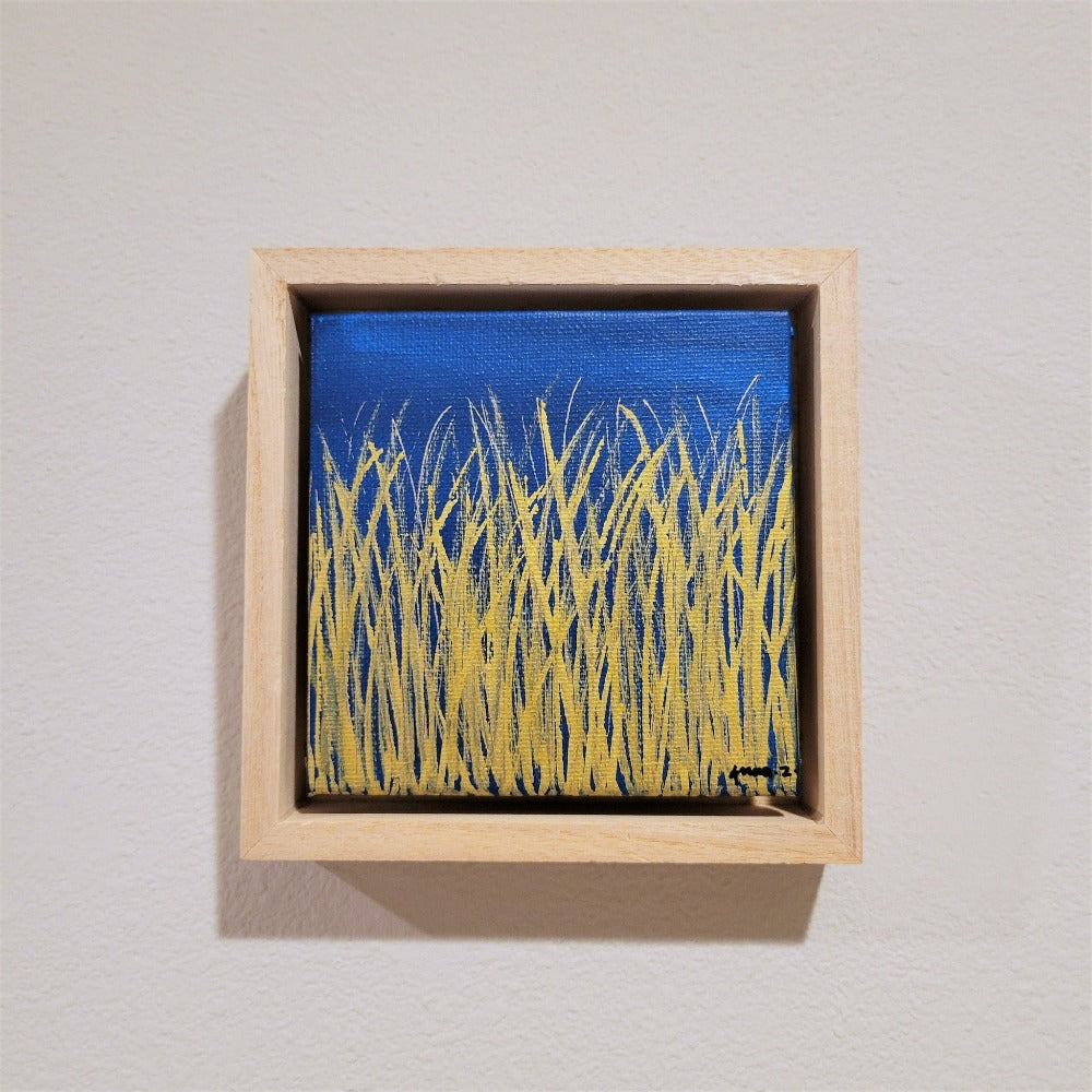 Golden blades of grass set against a bright blue  background on a framed mini-sized canvas panel. Metallic gold colored paint over acrylic.  Mounted in floater frame style within a 5" x 5" rustic wooden box frame with mini sawtooth hanger on reverse. The golden grass catches daylight beautifully and is perfectly complemented by the light colored wooden frame. 