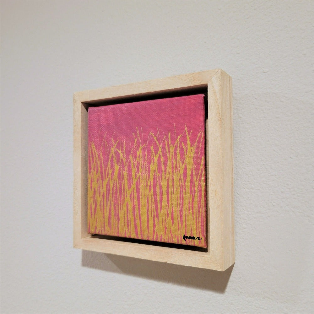 Golden blades of grass set against a bright pink background on a framed mini-sized canvas panel. Metallic gold colored paint over acrylic.  Mounted in floater frame style within a 5" x 5" rustic wooden box frame with mini sawtooth hanger on reverse. The golden grass catches daylight beautifully and is perfectly complemented by the light colored wooden frame. 