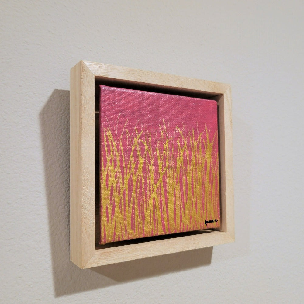 Golden blades of grass set against a bright pink background on a framed mini-sized canvas panel. Metallic gold colored paint over acrylic.  Mounted in floater frame style within a 5" x 5" rustic wooden box frame with mini sawtooth hanger on reverse. The golden grass catches daylight beautifully and is perfectly complemented by the light colored wooden frame. 
